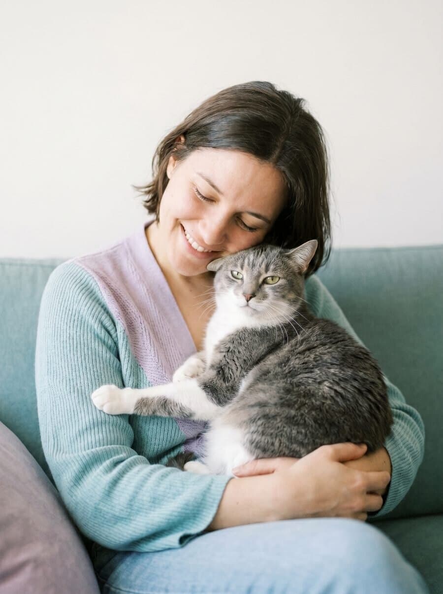 Tierhalterin sitzt auf dem Sofa und schmust mit ihrer Katze